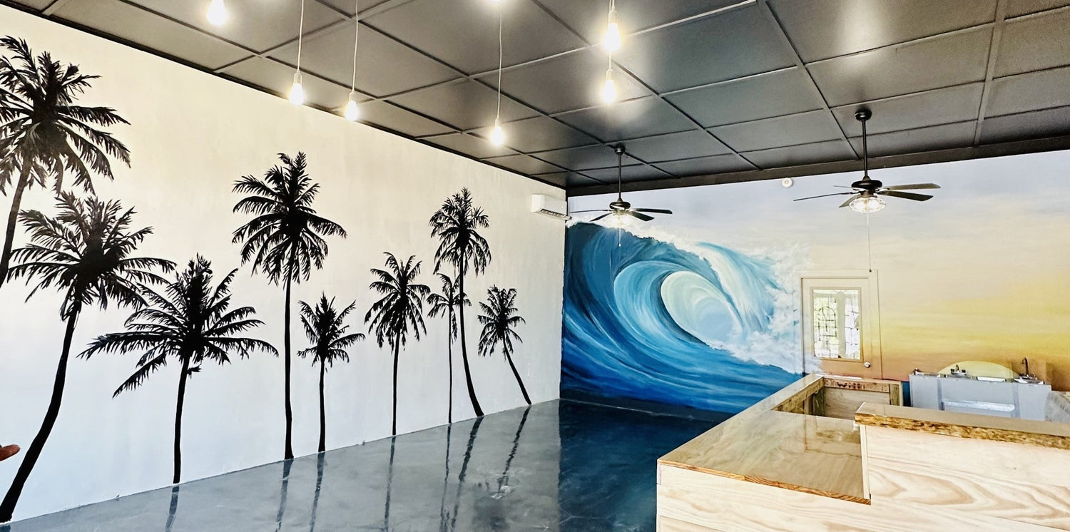 Modern office interior with palm tree and wave wall murals. Black and white trees contrasted with colorful sunset and bright blue giant wave mural on back wall