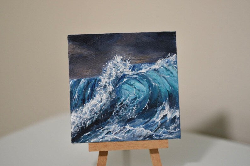 Painting of a wave on a small canvas, the background of the painting has dark stormy skies, the wave is crashing with a lot of white bubbles